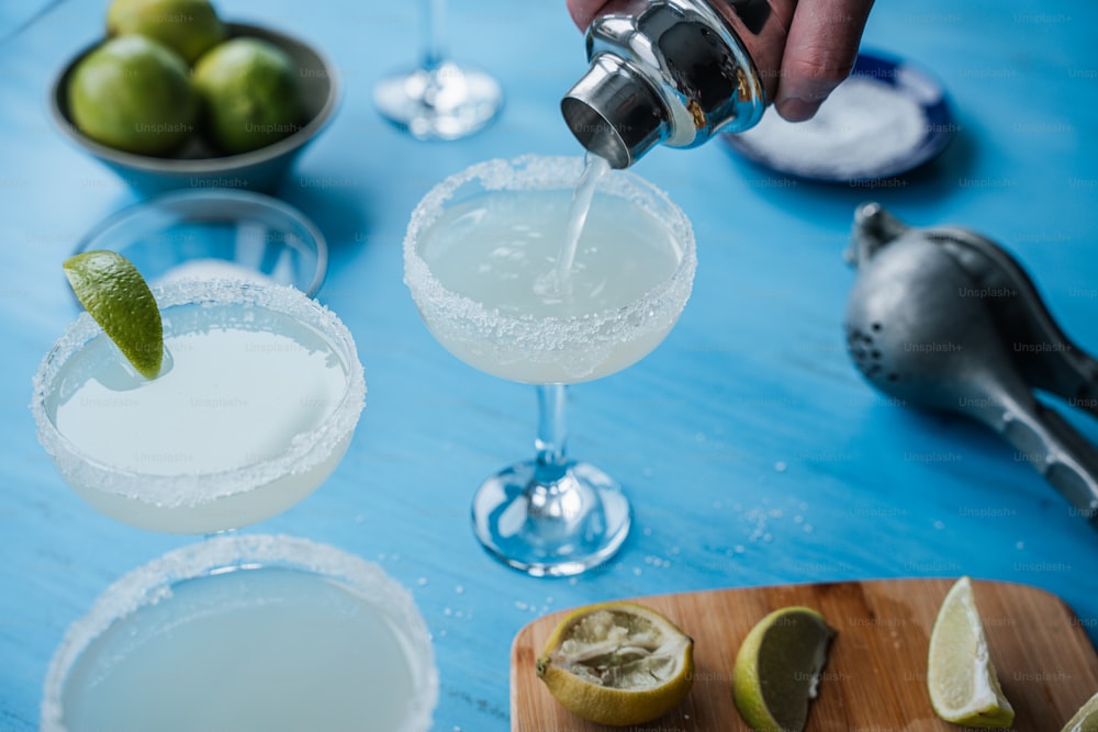 a person pours a drink into two margarita glasses