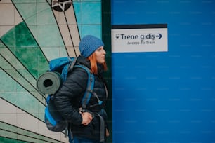 a woman with a blue backpack is standing in front of a blue wall