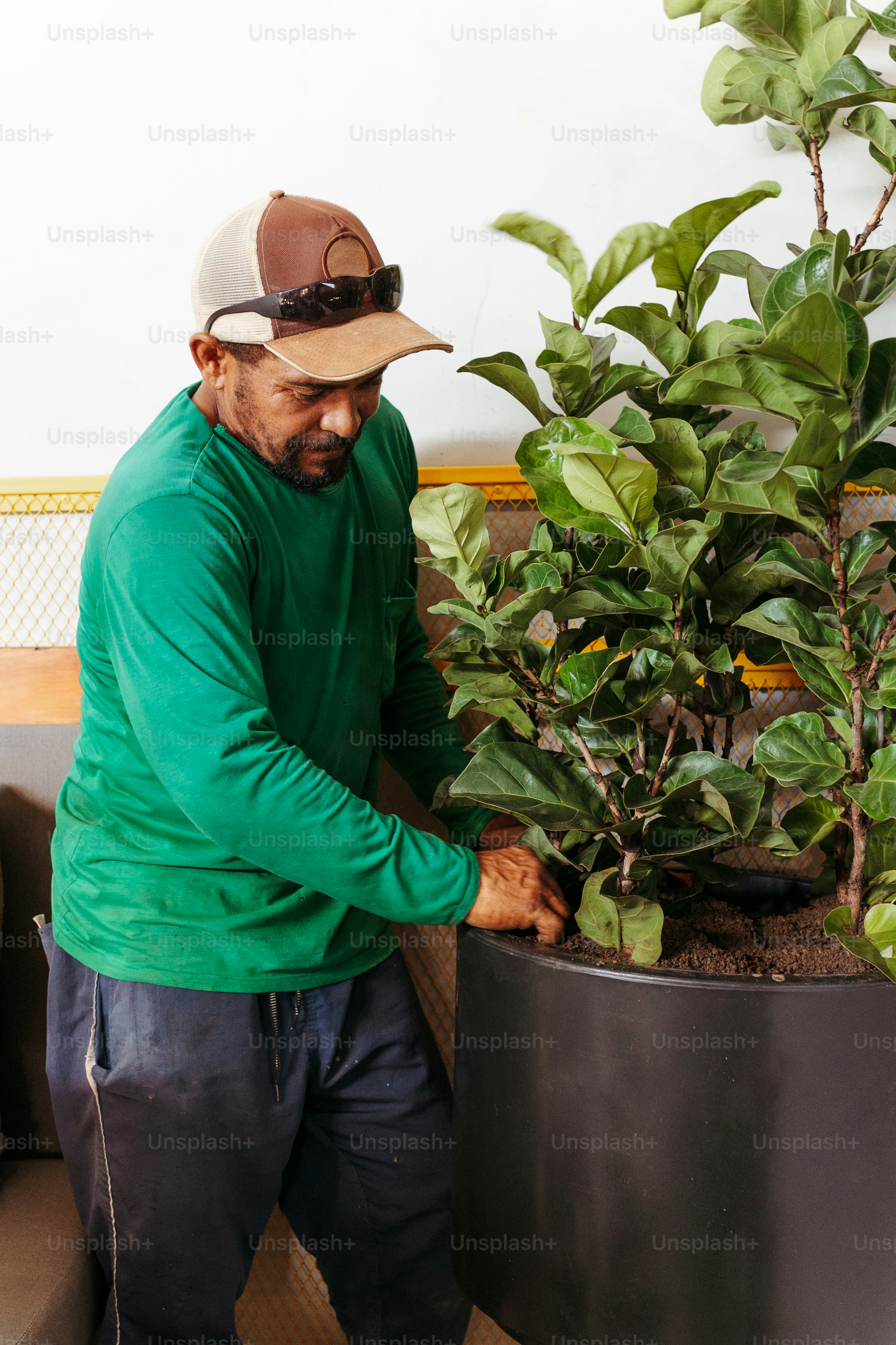 a man in a green shirt and hat standing next to a potted plant