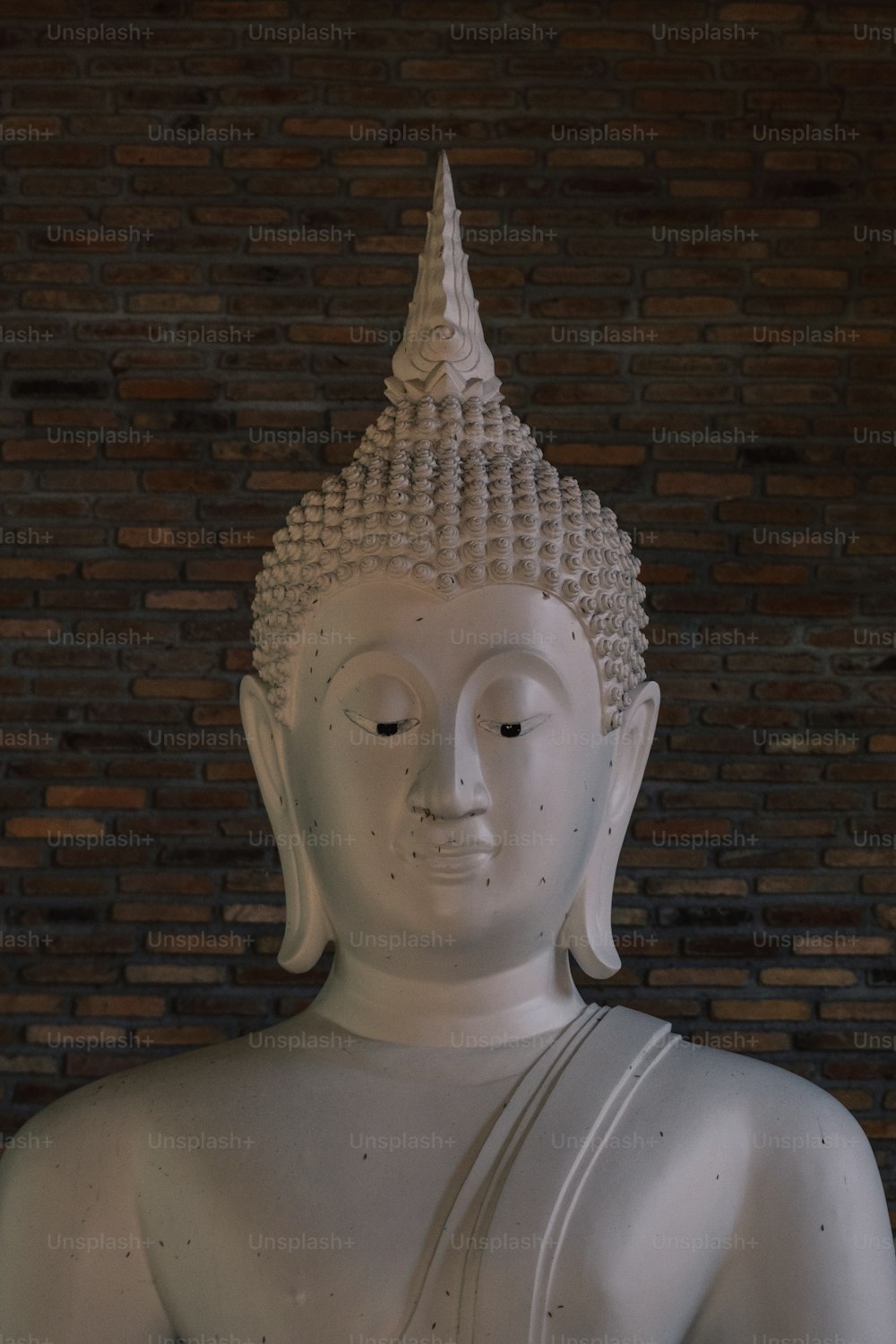 a white buddha statue sitting in front of a brick wall
