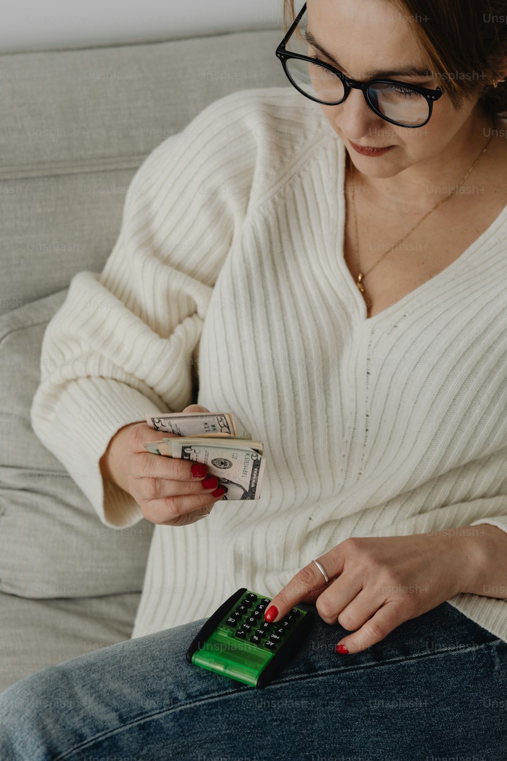 a woman sitting on a couch holding money and a cell phone