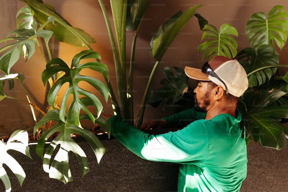 a man in a green shirt leaning against a plant