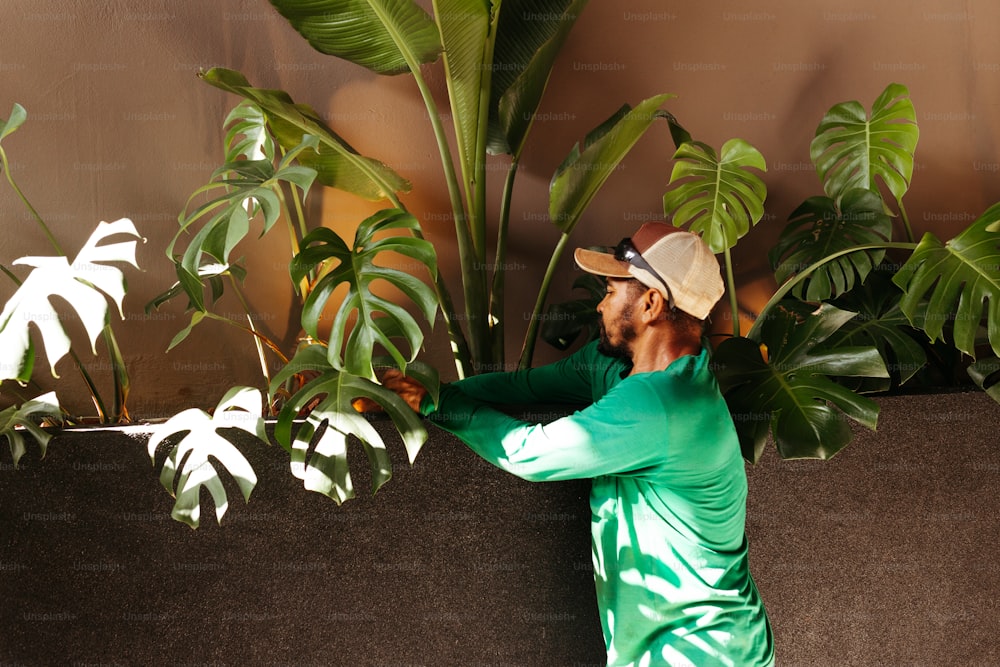 녹색 셔츠를 입고 모자를 쓴 남자가 식물 옆에 서 있다