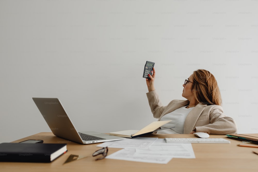 a woman sitting at a desk holding up a cell phone