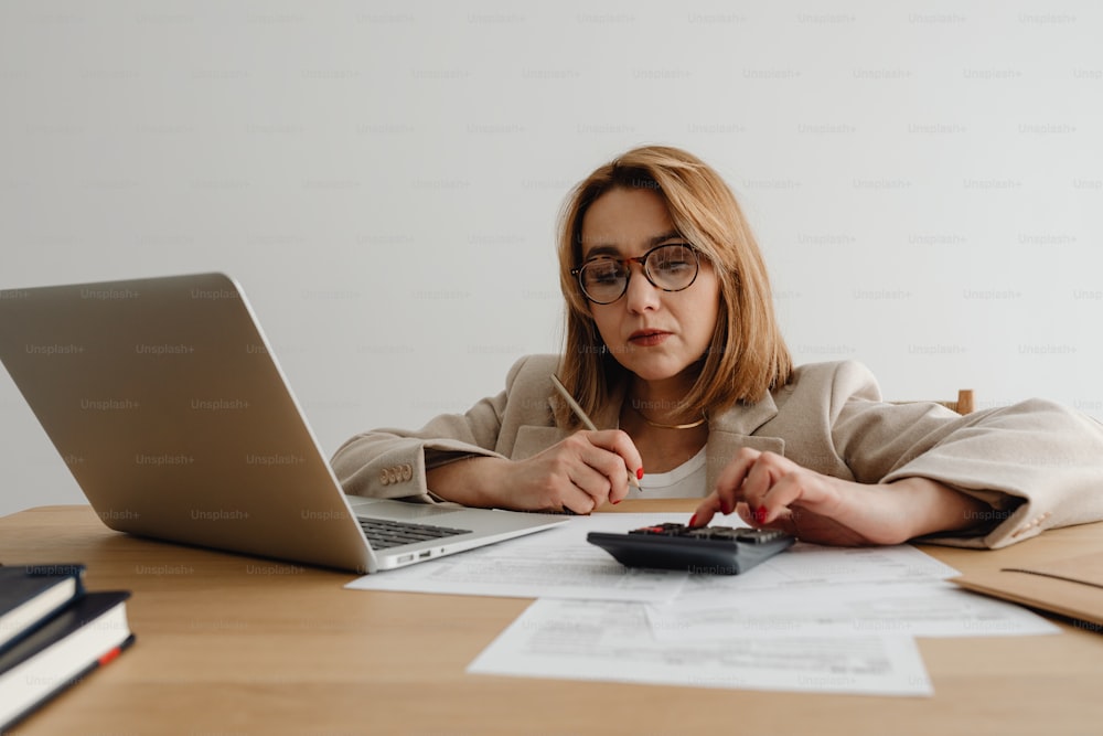 Eine Frau sitzt mit Laptop und Taschenrechner am Schreibtisch