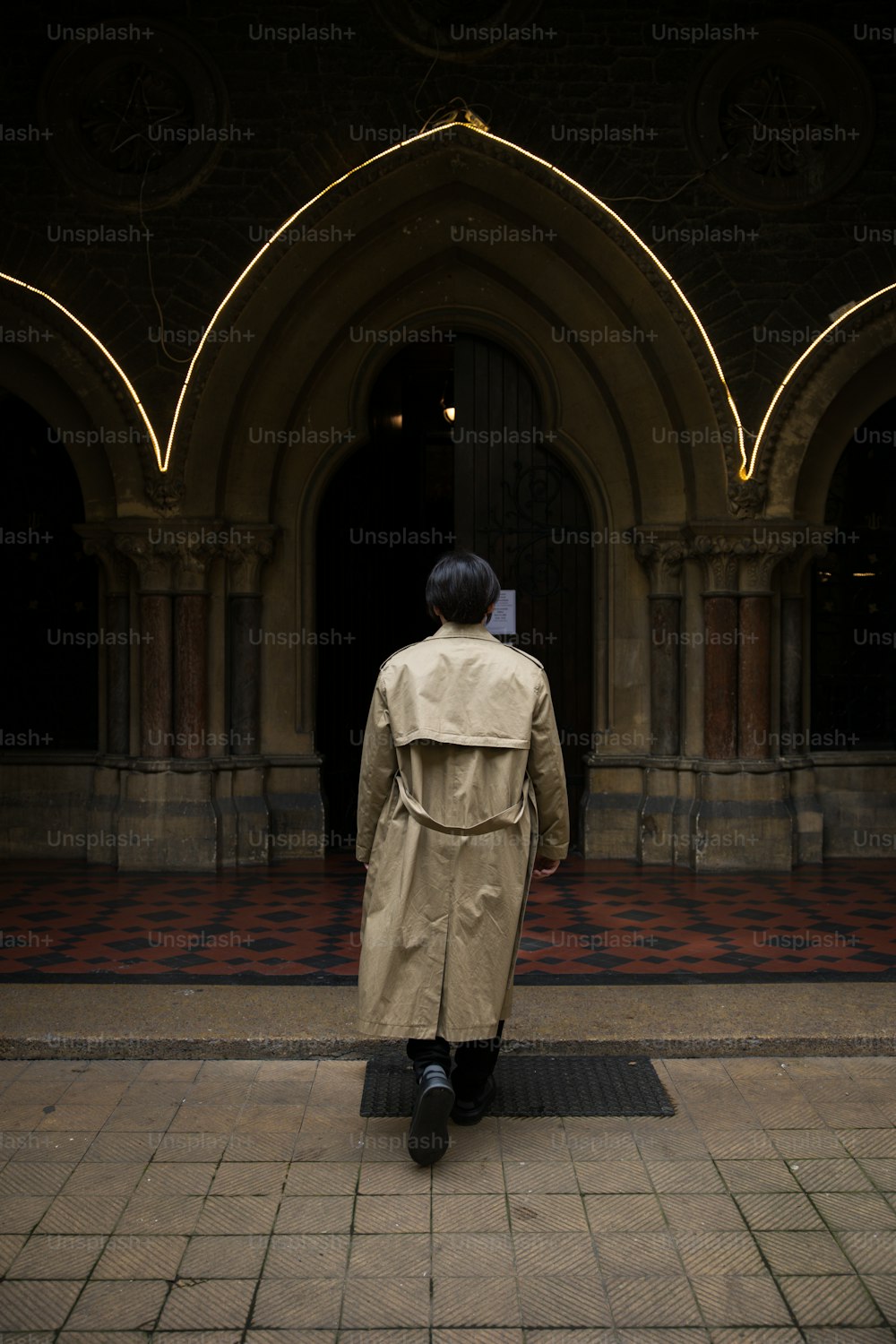 um homem em um casaco de trincheira está de pé na frente de um prédio