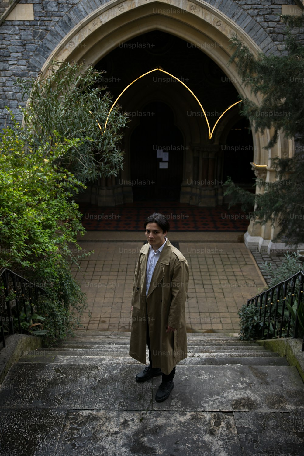 a man in a trench coat standing in front of a building