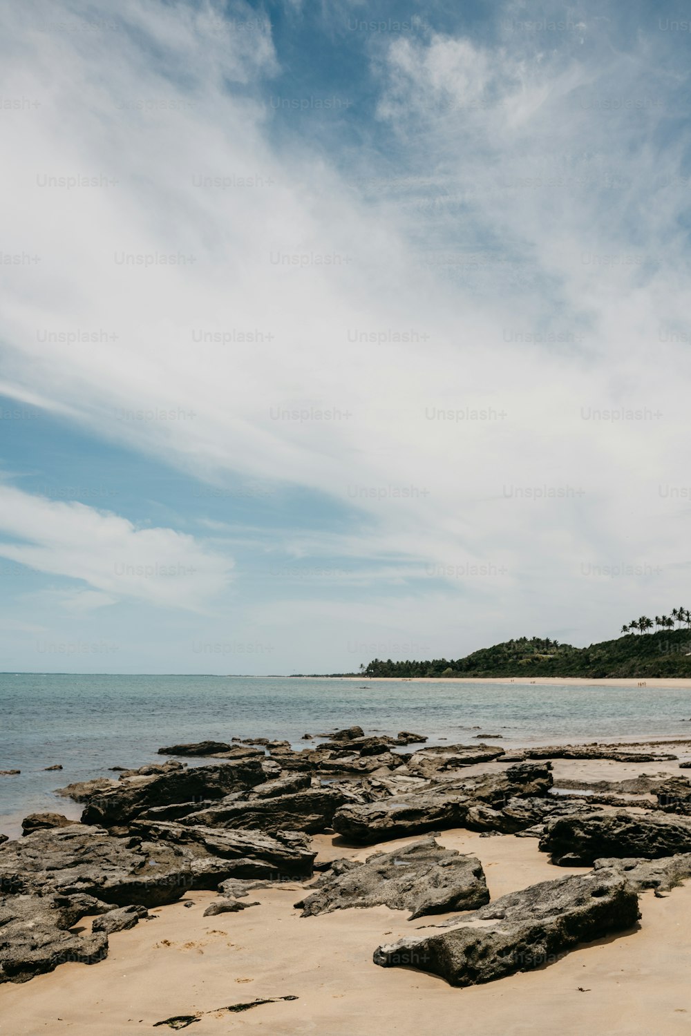 Una playa de arena con rocas y agua bajo un cielo azul nublado