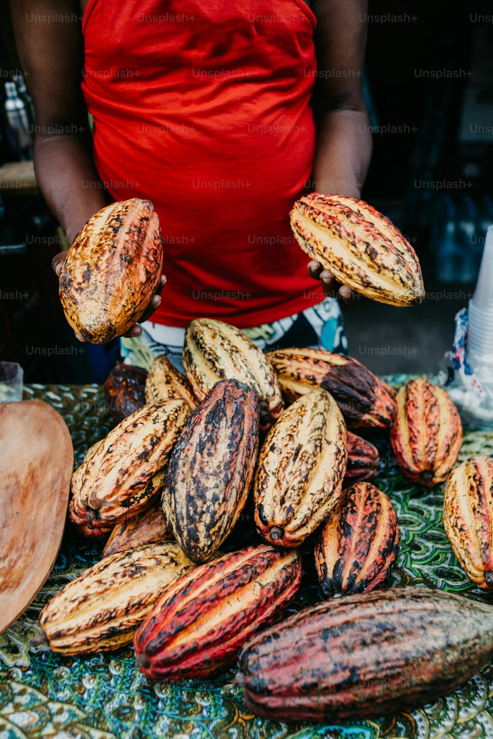 Une personne en chemise rouge debout à côté d’un tas de fèves de cacao