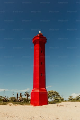 a red lighthouse on a sandy beach under a blue sky