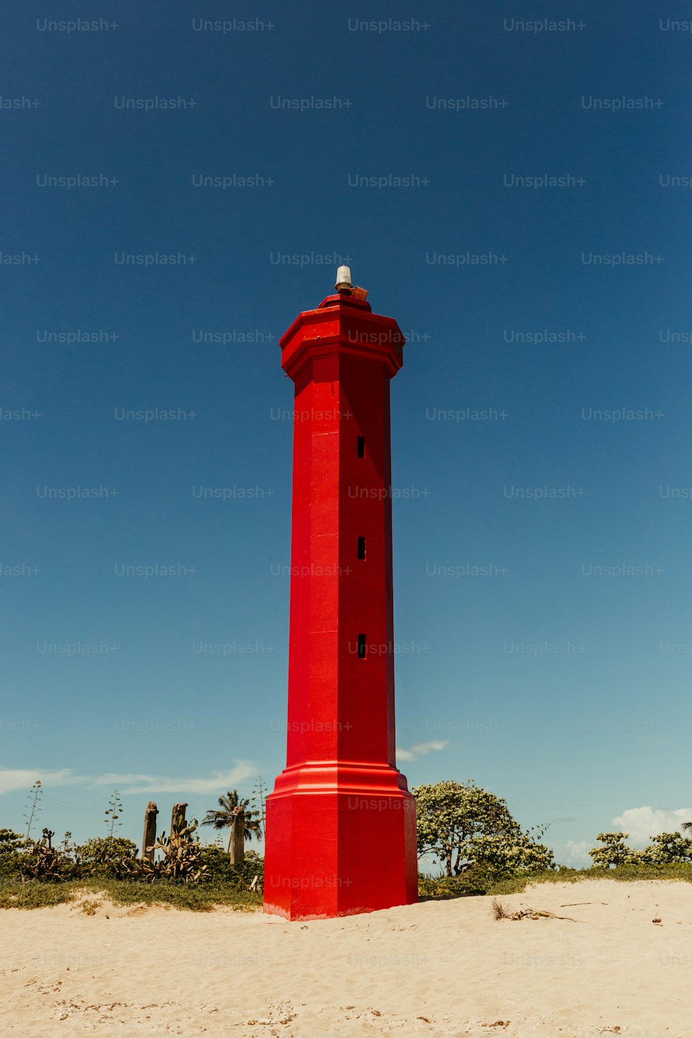 Ein roter Leuchtturm an einem Sandstrand unter blauem Himmel