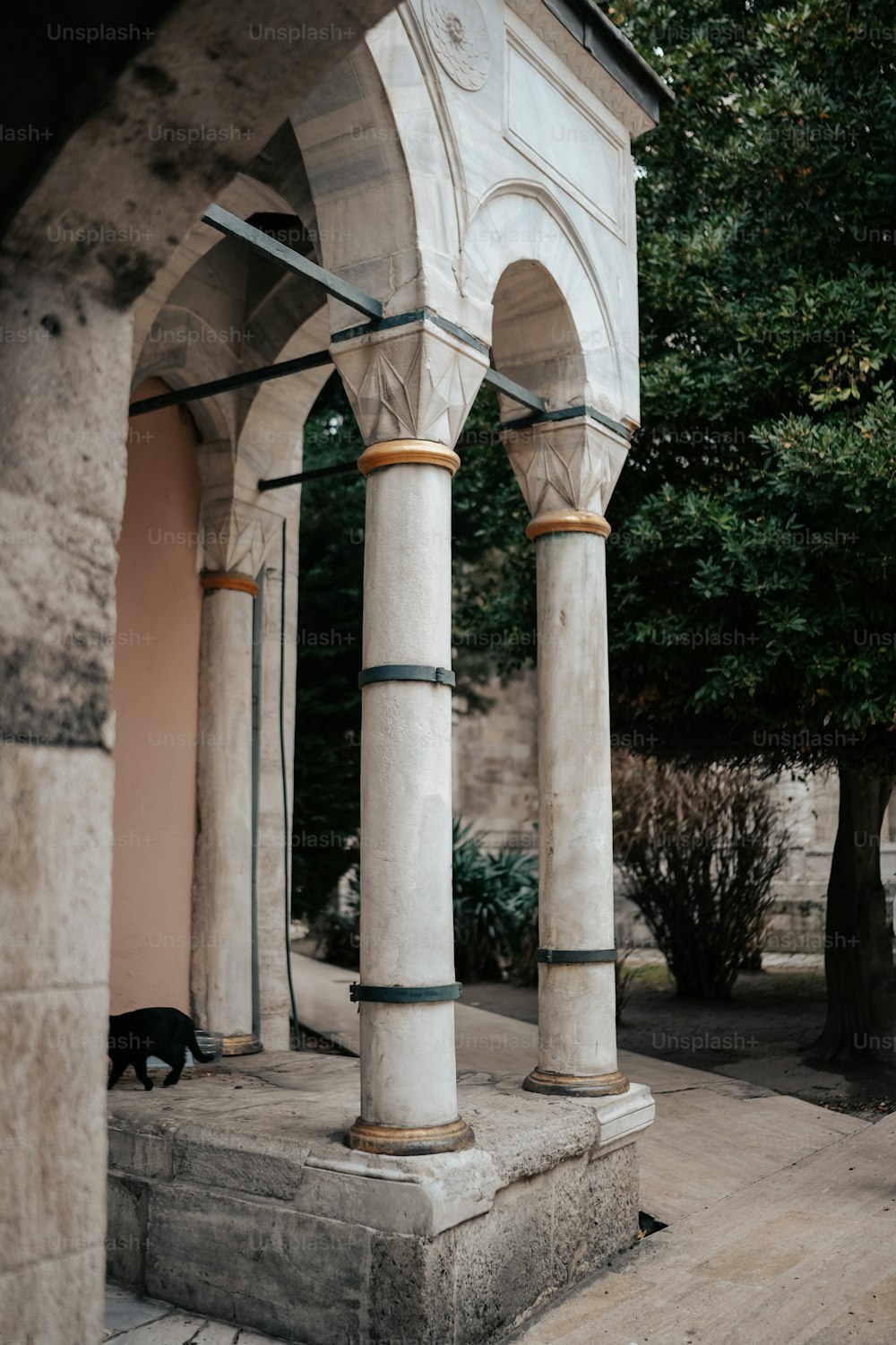 a cat sitting on the ground under a stone structure