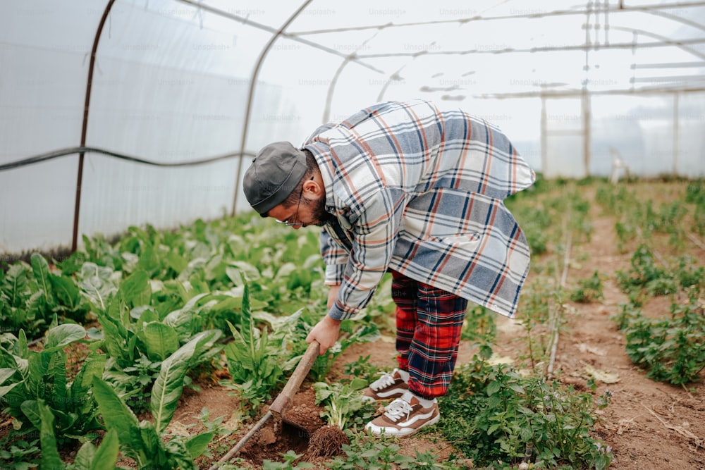 a man in a plaid shirt is digging in a garden