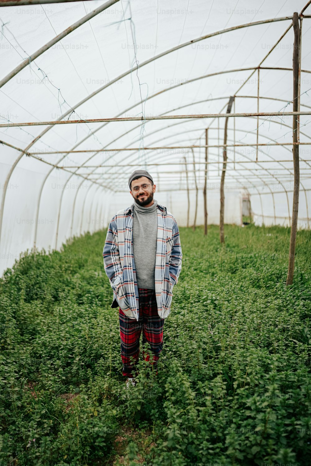 a man standing in a greenhouse wearing a plaid coat