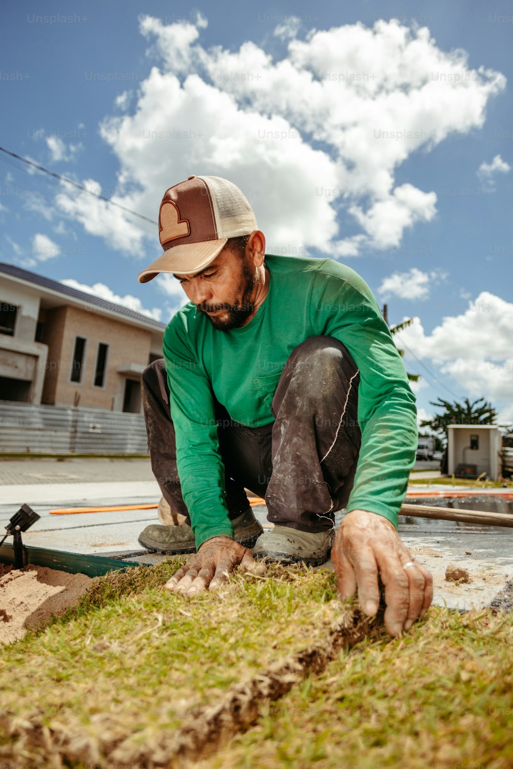 a man in a green shirt and hat working on grass