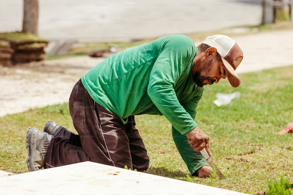 Un hombre con camisa verde y sombrero cavando en la hierba