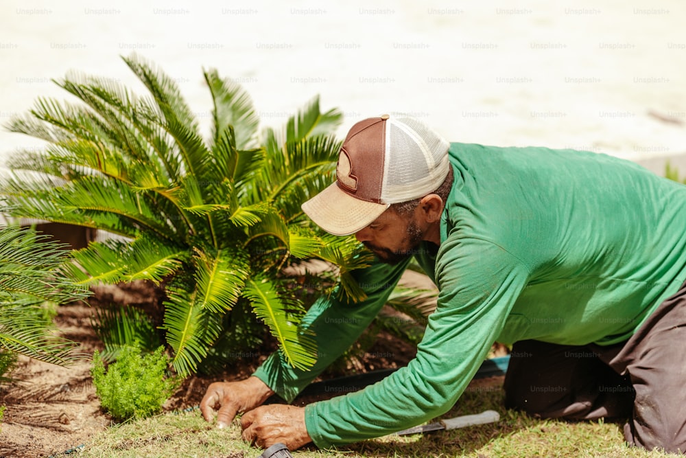 a man in a green shirt and hat working on a plant