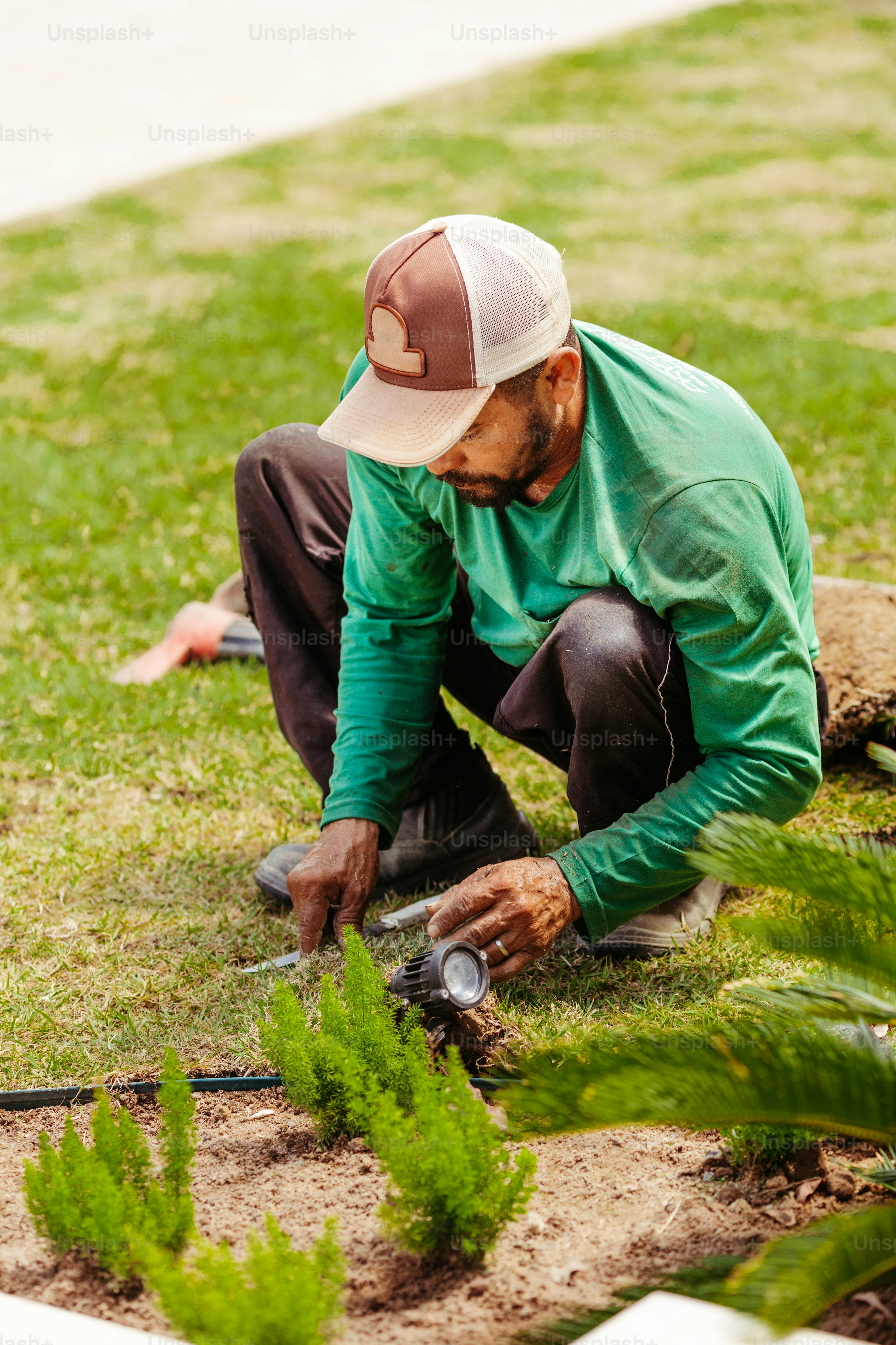A man in a green shirt and hat working in a garden photo – Gardening ...