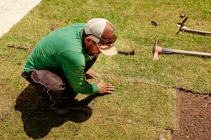 a man in a green shirt is working on a patch of grass