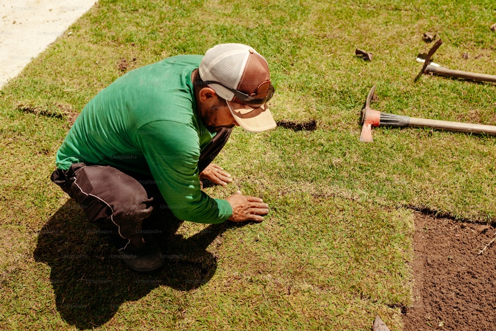a man in a green shirt is working on a patch of grass