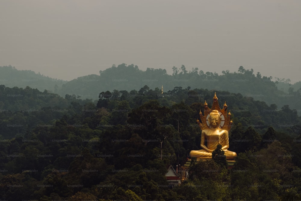 a large golden buddha statue sitting on top of a lush green forest