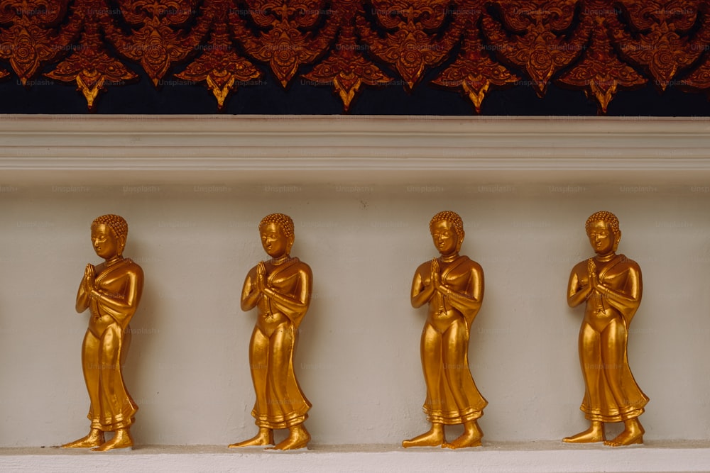 a row of golden buddha statues sitting on top of a white shelf