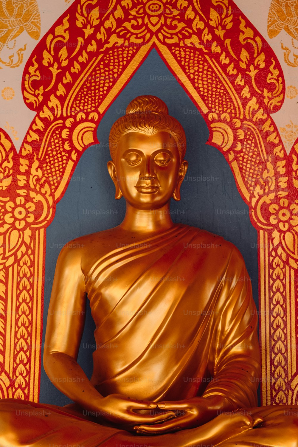 a golden buddha statue sitting in front of a red and gold wall