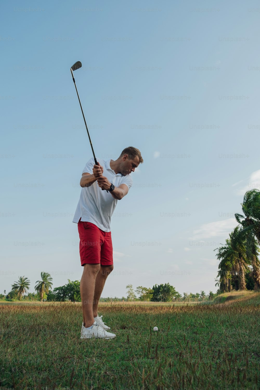 a man in a white shirt and red shorts playing golf