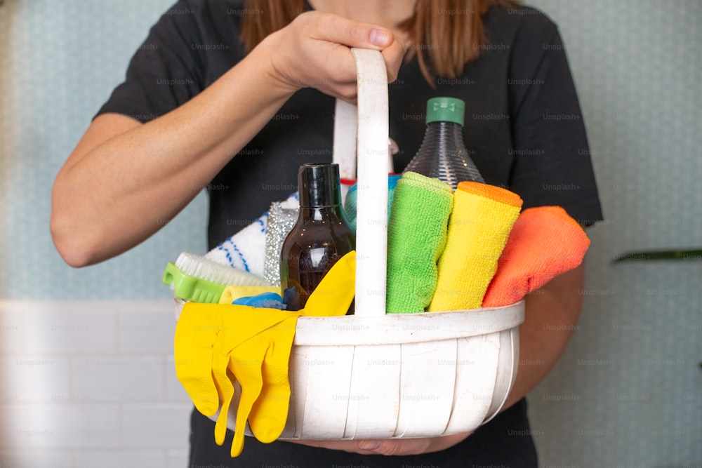 Una mujer sosteniendo una canasta de artículos de limpieza