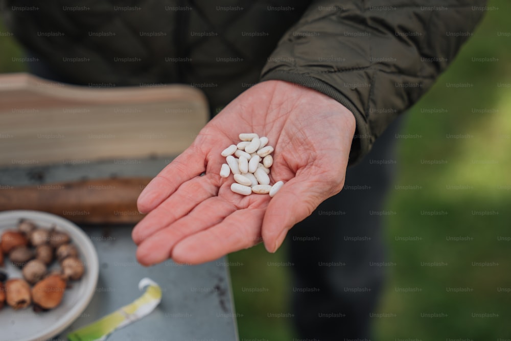 uma pessoa segurando um punhado de pílulas brancas em sua mão