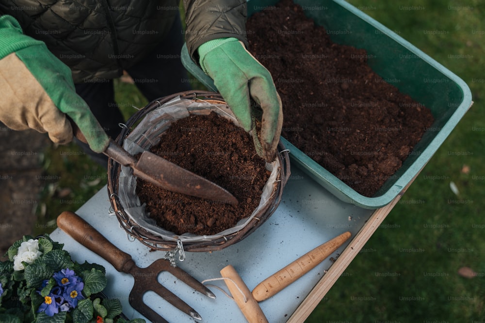 a person with gardening gloves and gloves scooping dirt into a bowl