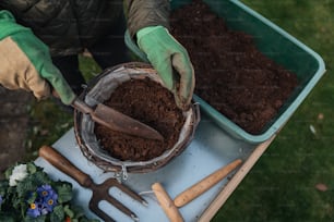 a person with gardening gloves and gloves scooping dirt into a bowl