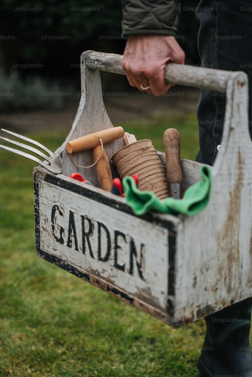 Una persona sosteniendo una caja de jardín llena de herramientas de jardinería