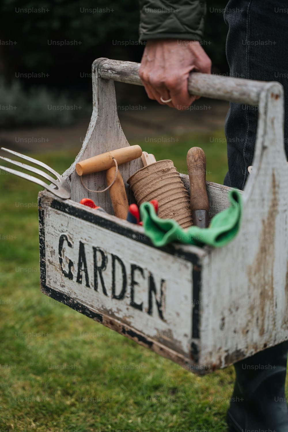 una persona che tiene una scatola da giardino piena di attrezzi da giardinaggio