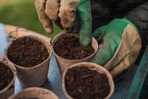 a person wearing gloves and gardening gloves scooping dirt into small pots
