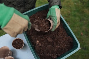 a person in green gloves is digging dirt into a container