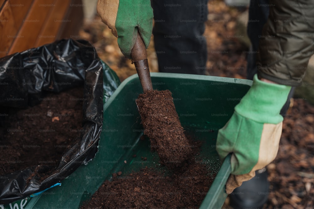 a person shoveling dirt into a green container