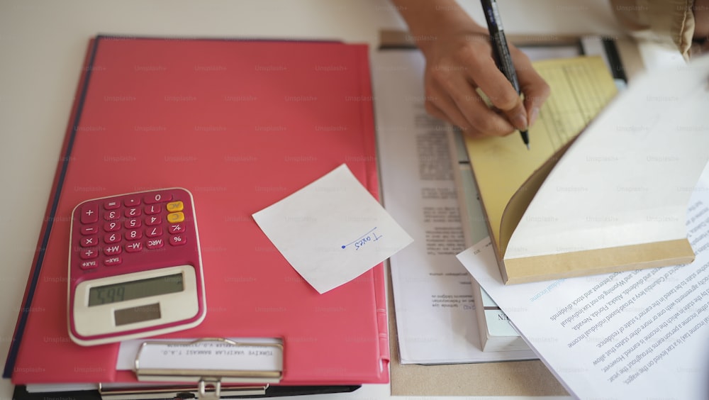 Una persona escribiendo en un pedazo de papel junto a una calculadora