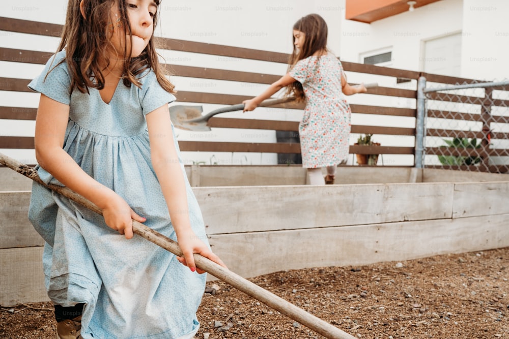 una niña sosteniendo una pala y una niña sosteniendo un palo