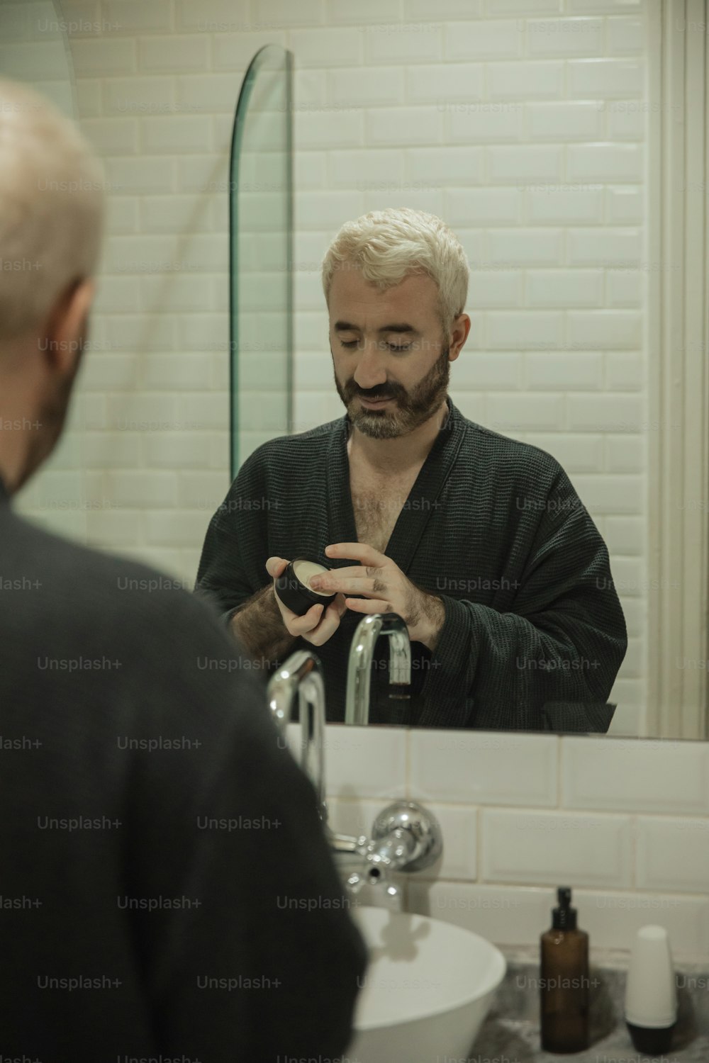 a man with a goatee is looking at his reflection in the mirror