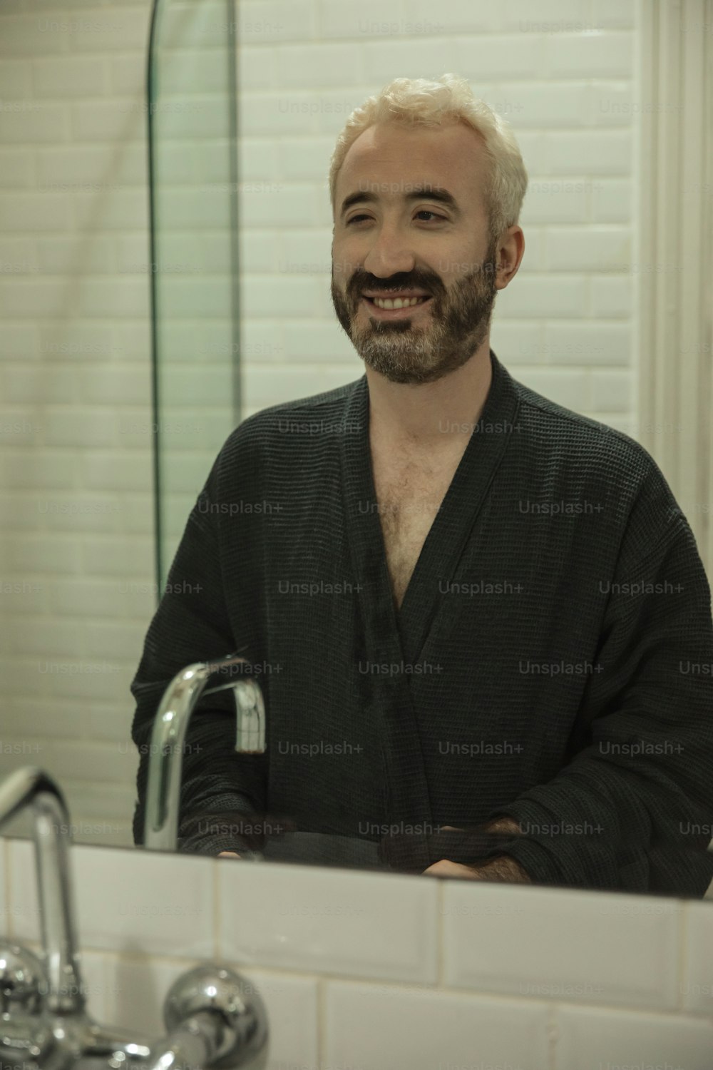 흰 머리와 수염을 가진 남자가 욕실 거울 앞에 서 있다