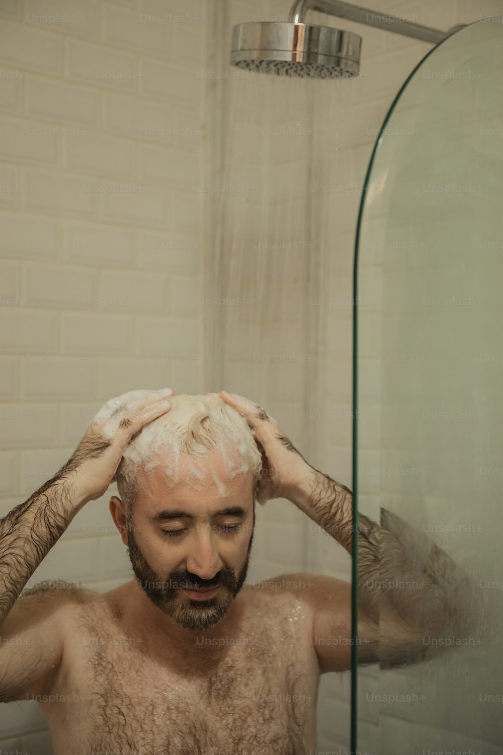 Ein hemdloser Mann mit Bart steht unter der Dusche