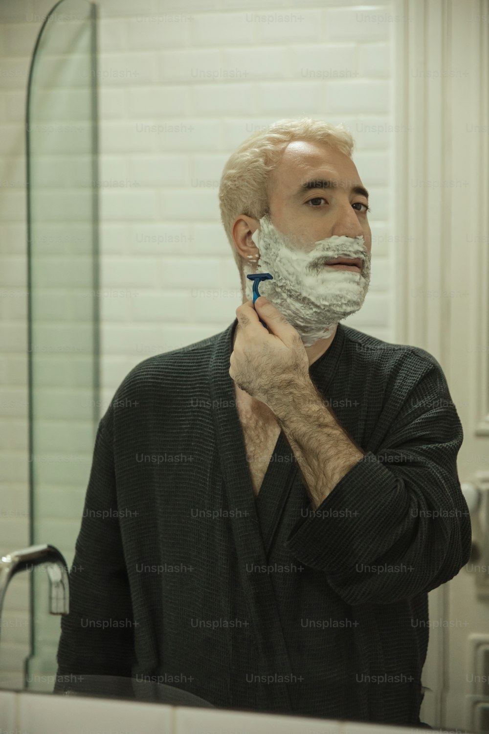 a man shaving his face in a bathroom mirror