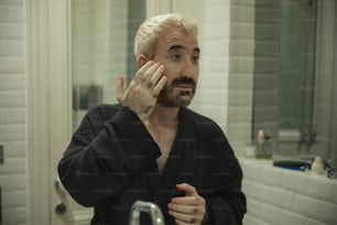 a man in a bathrobe brushing his teeth in front of a mirror