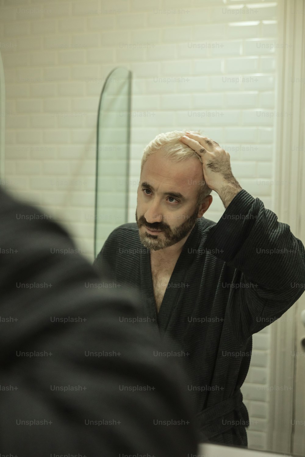a man with a goatee combing his hair in front of a mirror