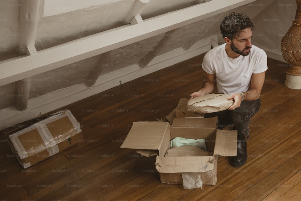 Un uomo seduto sul pavimento con in mano una scatola
