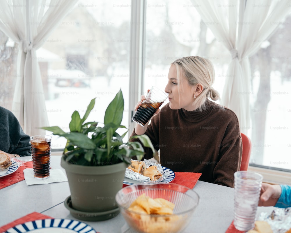 a woman sitting at a table drinking from a cup