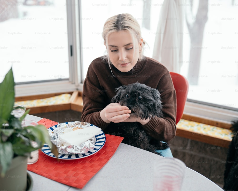 eine Frau, die mit einem Kuchen und einem Hund an einem Tisch sitzt