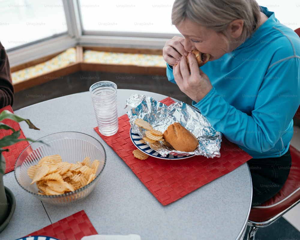 uma mulher sentada em uma mesa comendo um sanduíche e batatas fritas
