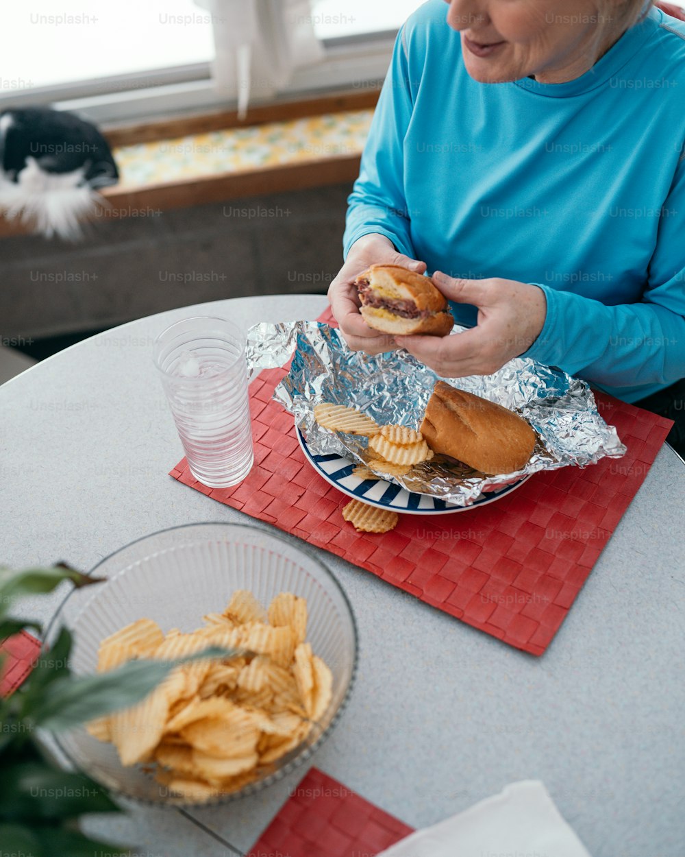 uma mulher sentada em uma mesa comendo um sanduíche e batatas fritas